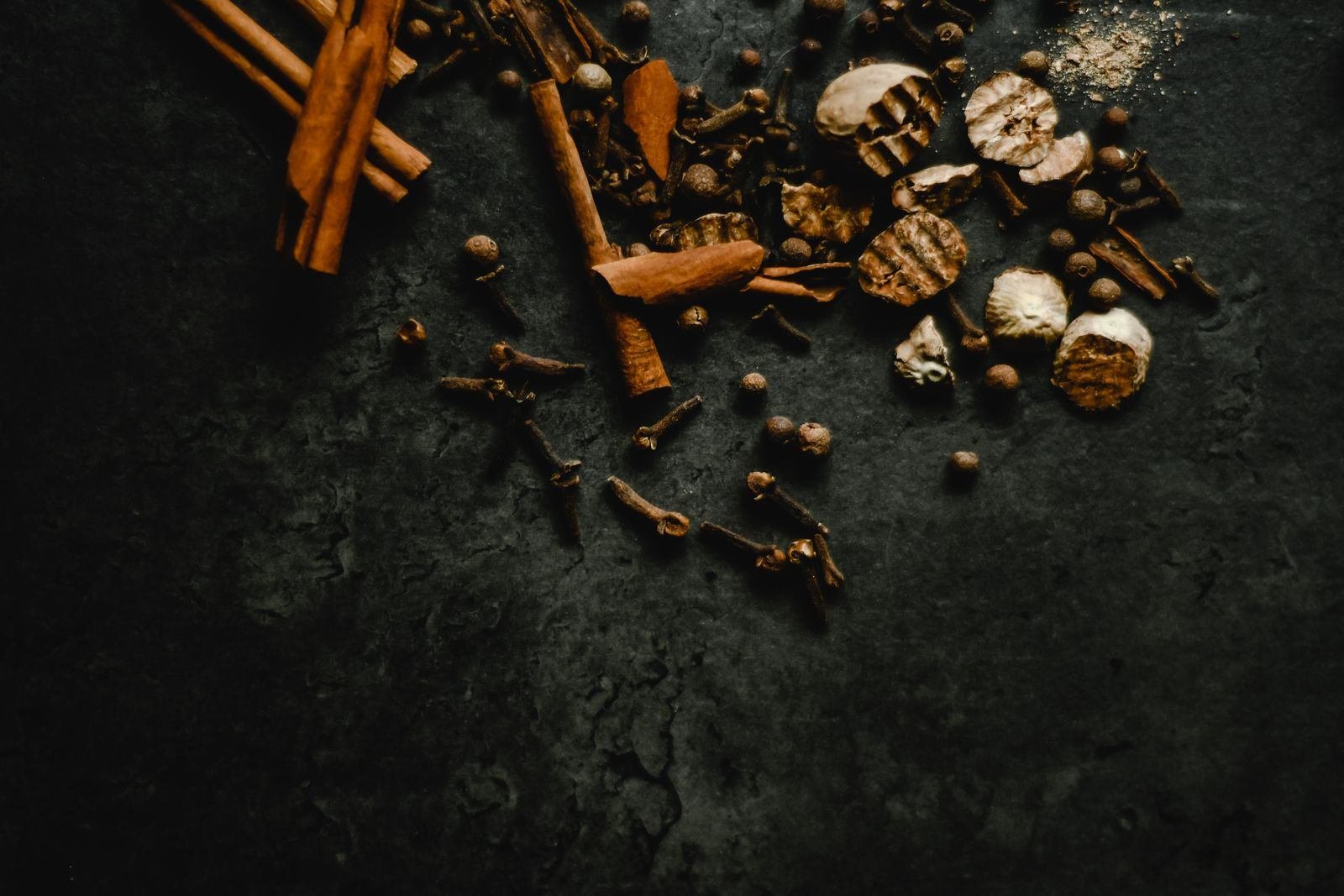 Cinnamon, cloves and nutmeg scattered on dark slate